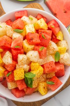 watermelon and pineapple salad in a white bowl with mint sprinkled on top