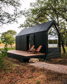 a small black cabin sitting on top of a wooden deck next to trees and grass