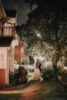 a bride and groom standing in front of a house at night with the lights on