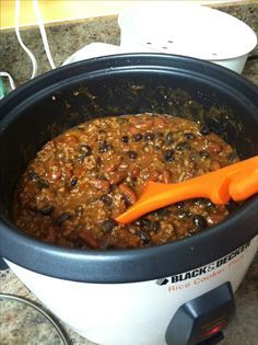 a crock pot filled with chili and beans next to an orange handled utensil