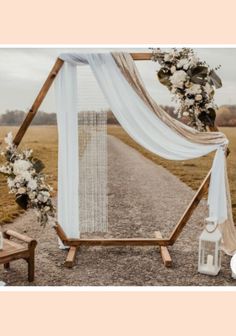 an outdoor ceremony setup with white drapes and flowers on the side walk, along with two wooden benches