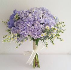 a bouquet of purple and white flowers in a vase on a table with a ribbon tied around it