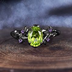 a ring with an oval cut green stone surrounded by purple and white stones on a wooden surface