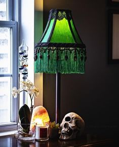 a green lamp sitting on top of a wooden table next to a skull and flowers