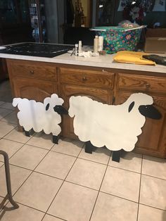 two paper cut out sheep standing on the floor next to a counter top in a kitchen