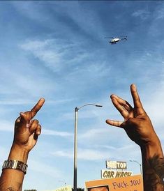 two hands making the peace sign with an airplane in the sky above them and another hand reaching up