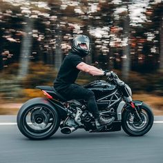 a man riding on the back of a black motorcycle down a road with trees in the background