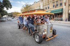 a group of people riding on the back of an orange and silver vehicle down a street