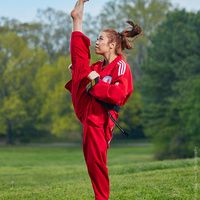 a woman in red is doing karate on the grass