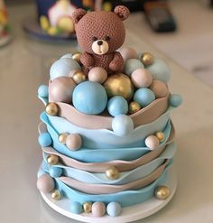 a teddy bear sitting on top of a blue and white cake with gold balls around it