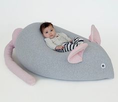 a baby laying on top of a gray pillow with a pink fish shaped cushion around it