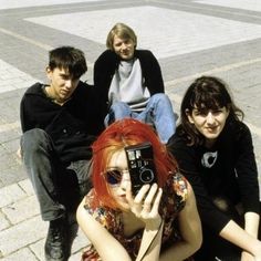 four people sitting on the ground with one holding a camera in front of her face