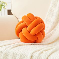 an orange knot pillow sitting on top of a white couch