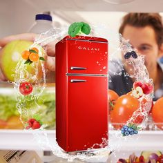 a red refrigerator freezer sitting inside of a kitchen next to fruits and vegetables in front of a man