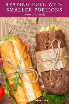 a sandwich wrapped in brown paper next to another sandwich on top of a wooden table