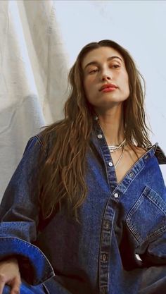 a woman with long hair sitting on the floor wearing a denim shirt and jeans pants