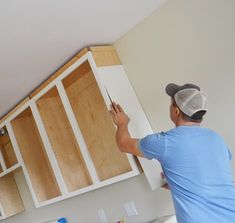 a man in blue shirt and cap painting cabinets with white paint on the wall behind him