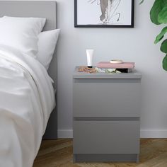 a nightstand next to a bed with a plant on it and a painting hanging above