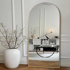 a white vase sitting next to a large mirror on top of a wooden flooring