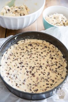 a pan filled with batter and chocolate chips on top of a wooden table next to two bowls