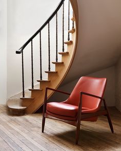 a red chair sitting in front of a spiral stair case next to a wooden handrail