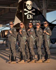 the women are posing for a photo in front of an air force fighter jet with skull decorations on it