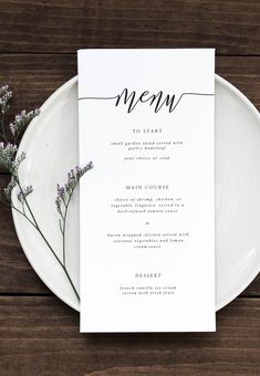 a white plate topped with a menu on top of a wooden table next to a purple flower