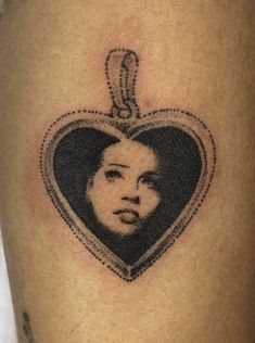 a woman's face in a heart - shaped frame tattoo on the thigh,