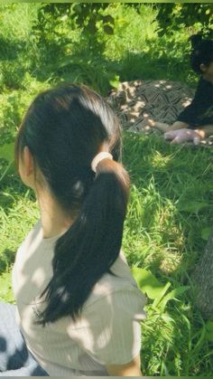 a woman sitting in the grass next to a tree