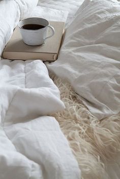 a cup of coffee sitting on top of a white blanket next to an open book