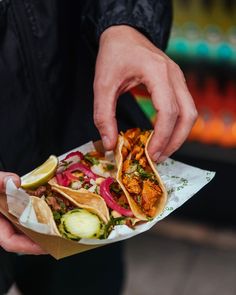 a person is holding some tacos with meat and veggies on it while wearing a black jacket