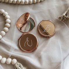 three compact mirrors sitting on top of a bed next to beads and a tassel