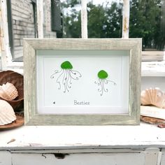 an old frame with two green jellyfishs on it and seashells in the background