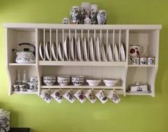 a white shelf filled with lots of dishes next to a wall mounted dish rack on top of a green wall