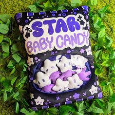 a purple and black star baby candy bag laying on the ground next to some green leaves