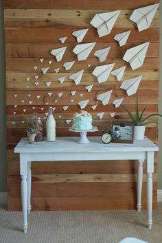 a white table topped with a cake next to a wall covered in paper boats and other decorations