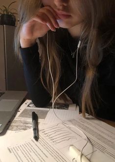 a woman sitting at a table with headphones on her ears and looking down while listening to music