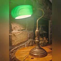 a green lamp sitting on top of a wooden table next to a stone wall and potted plant