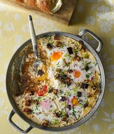 an omelet with eggs and vegetables in a pan on a table next to bread