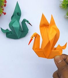 someone holding an origami swan next to another paper bird on a white surface