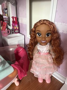 a doll in a pink dress standing next to a bathroom sink and mirror with her hair pulled back