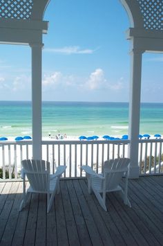 two white chairs sitting on top of a wooden deck next to an ocean and beach