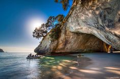 two people in a small boat on the water next to a large rock formation with trees growing out of it