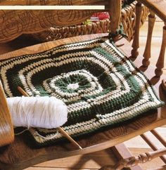 a crocheted rug sitting on top of a wooden rocking chair next to a ball of yarn