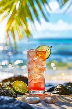 a drink sitting on top of a sandy beach next to the ocean with a slice of lime