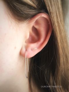 a close up of a person wearing a pair of silver hoop earrings on their ear