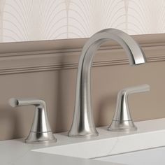 a bathroom sink with two faucets and a white counter top in front of a beige wall