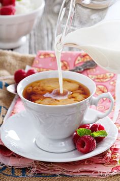 a white cup filled with liquid next to raspberries