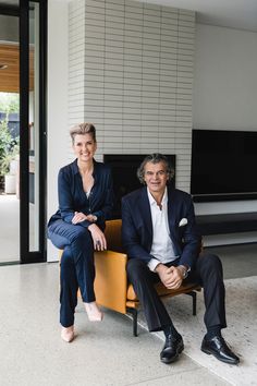 two people sitting on a chair in front of a fireplace