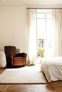 a bedroom with a bed, chair and window in the background that says a home in paris